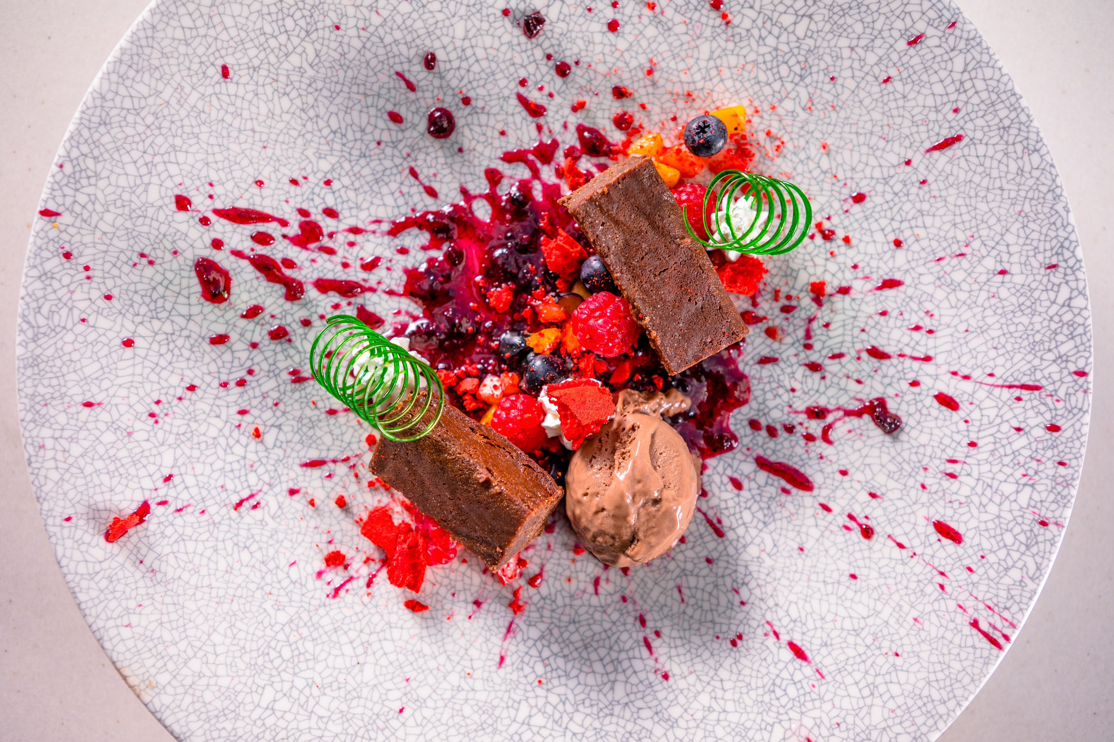 A dessert plate with chocolate pieces, berries, and a scoop of ice cream.