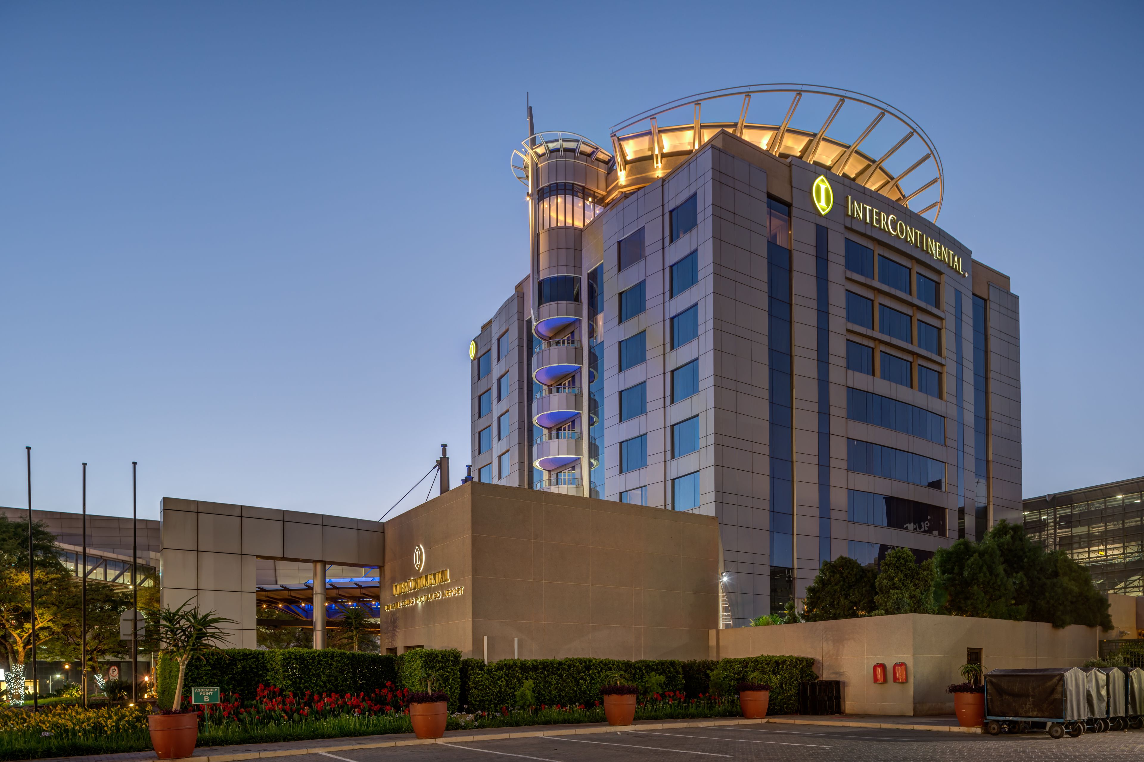 A modern hotel with a prominent circular tower, multiple balconies, and a well-lit entrance.