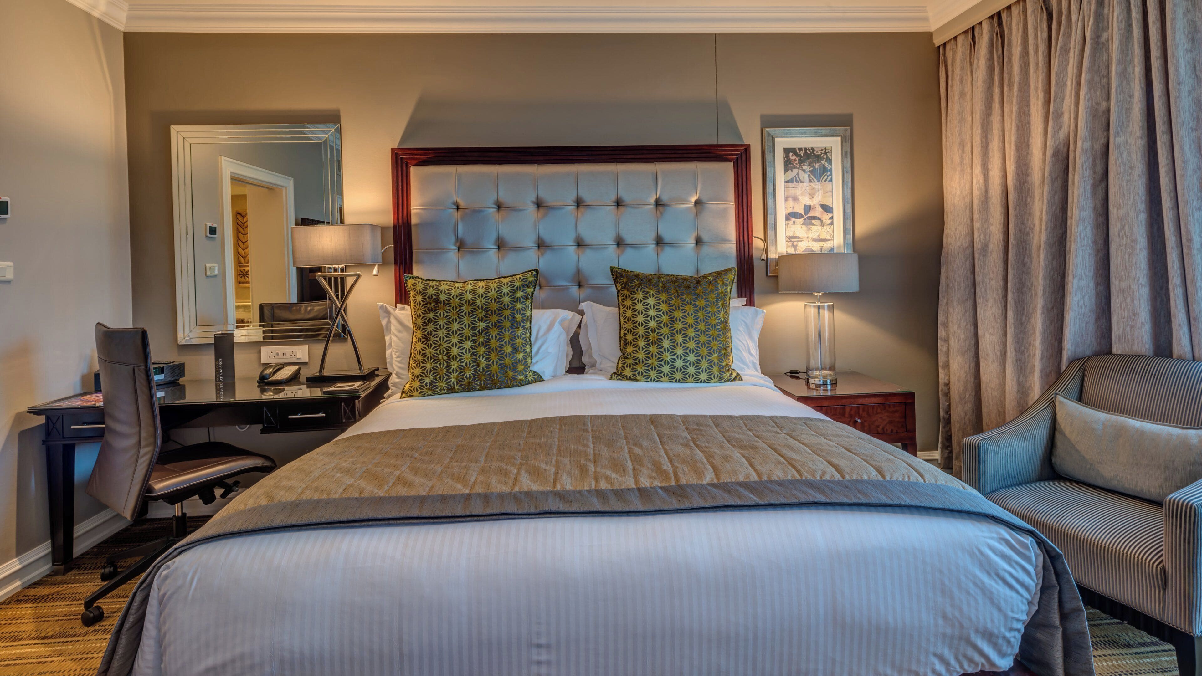 A hotel room with a large bed, a desk with a telephone, a chair, a lamp, and a picture on the wall.