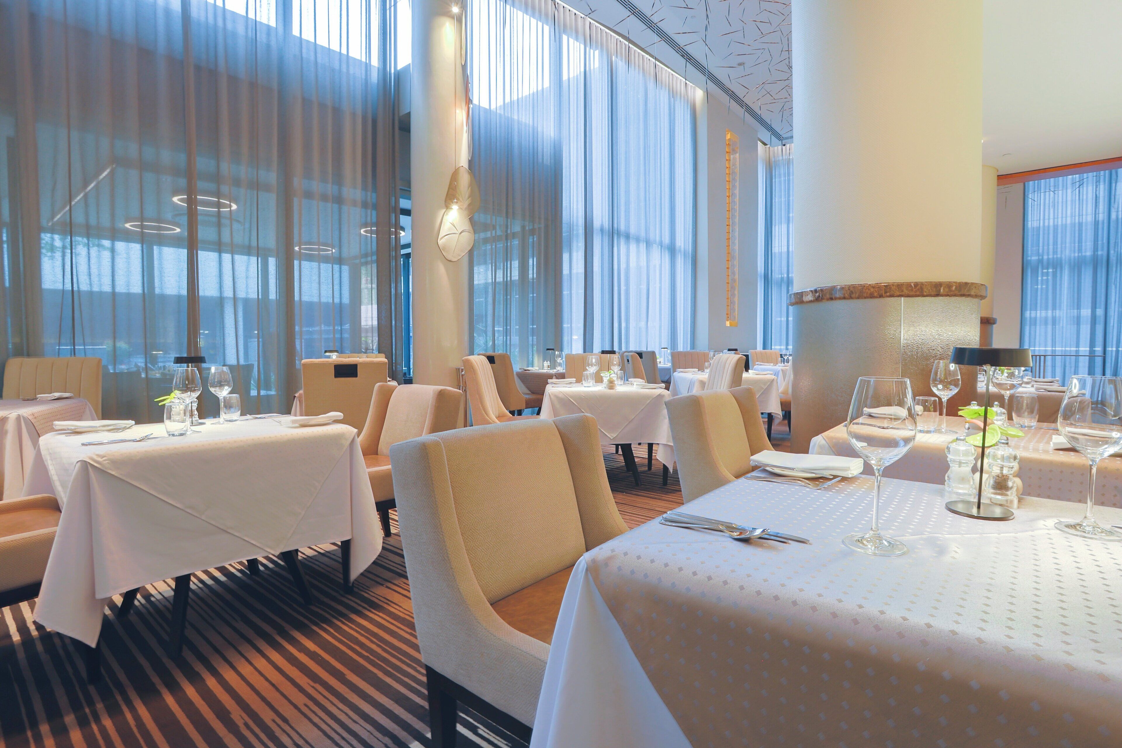 Un restaurante con varias mesas dispuestas para comer, ventanas amplias y diseño de interiores moderno.