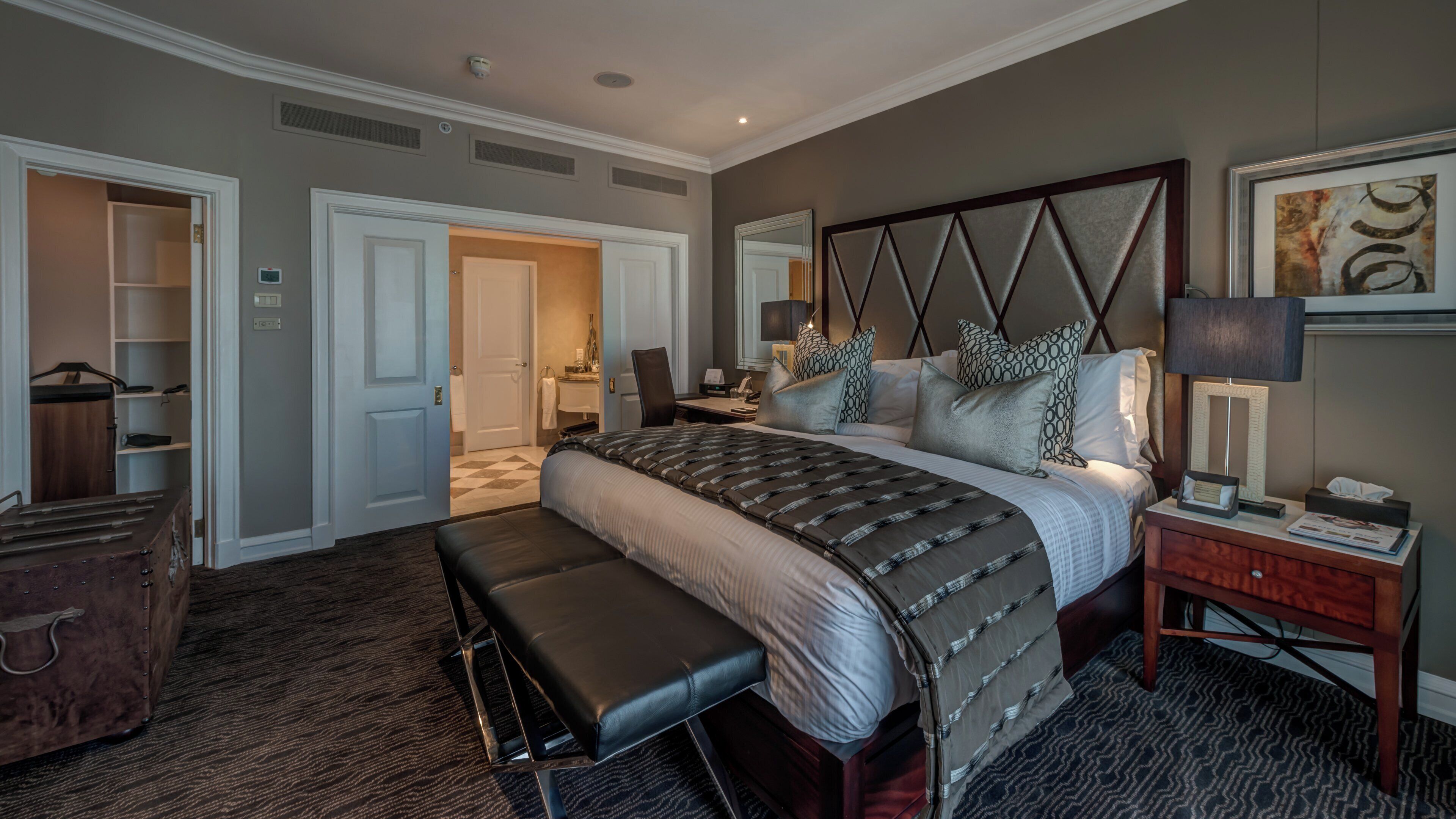 Una habitación de hotel con una cama grande, un banco, un escritorio y un armario.
