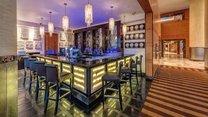 Zona de bar moderna con una barra central, taburetes y una iluminación decorativa.