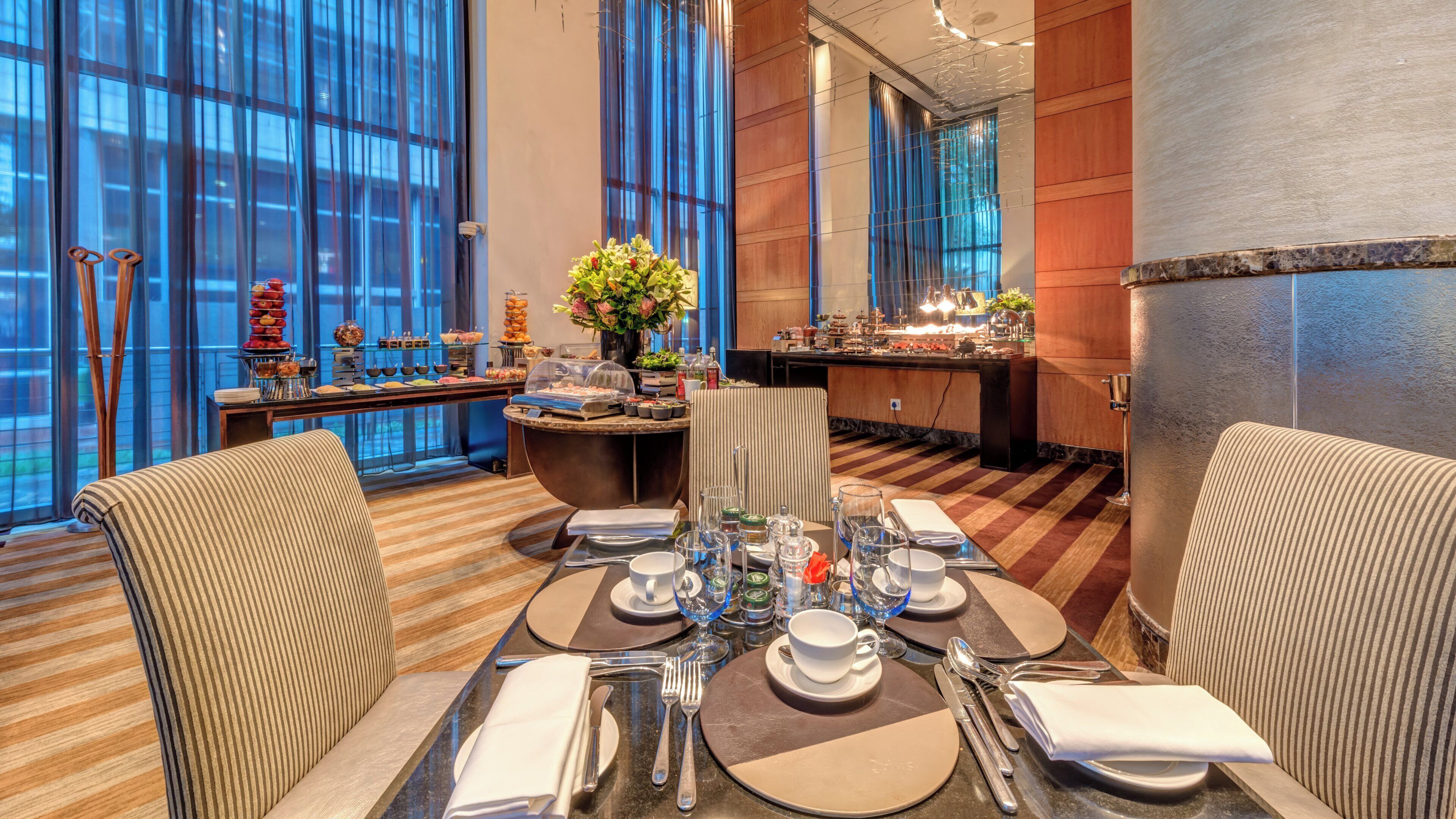 A hotel dining area with a buffet, a bar, and a seating arrangement with tables set for guests.