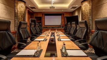 Un salón de conferencias con una larga mesa, sillas de cuero negro y una pantalla para proyector.