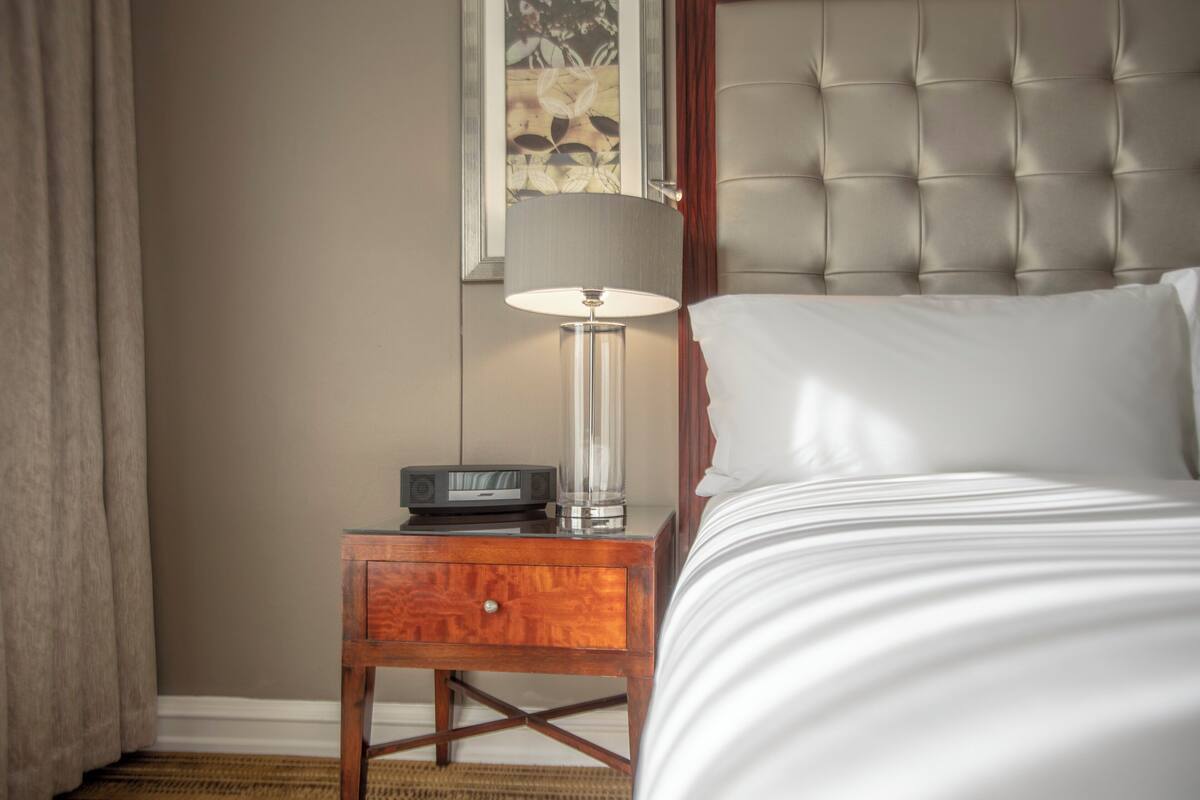 Une chambre à coucher avec un lit, une table de chevet avec une lampe et une œuvre d’art encadrée accrochée au mur.