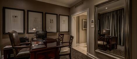 A hotel room with a desk, chair, and a large mirror. There are framed artworks on the wall and a carpeted floor.