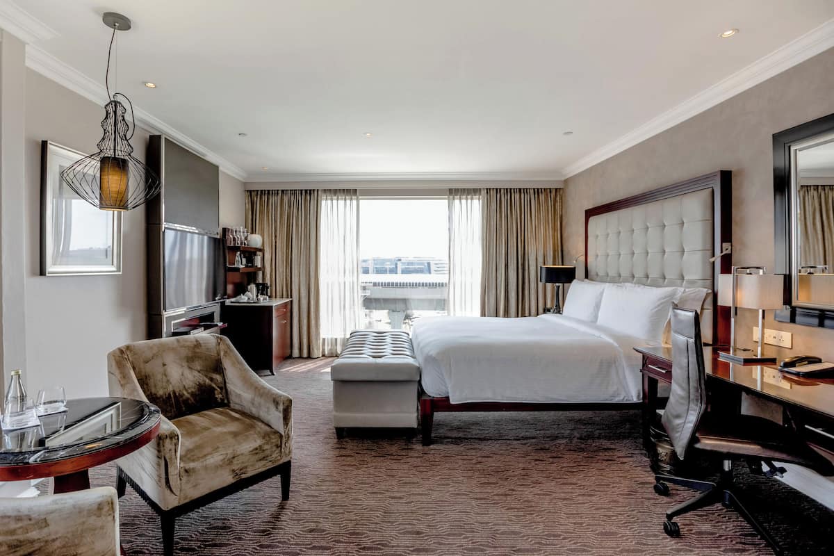 Une chambre d’hôtel avec un lit, une chaise, un bureau, une télévision et une grande fenêtre avec des rideaux.