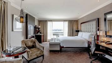 A hotel room with a bed, a chair, a desk, a TV, and a large window with curtains.
