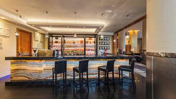 A modern bar area with a marble countertop, multiple bar stools, and a well-stocked liquor display.