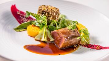 A plated dish with a piece of meat, vegetables, and a sauce.