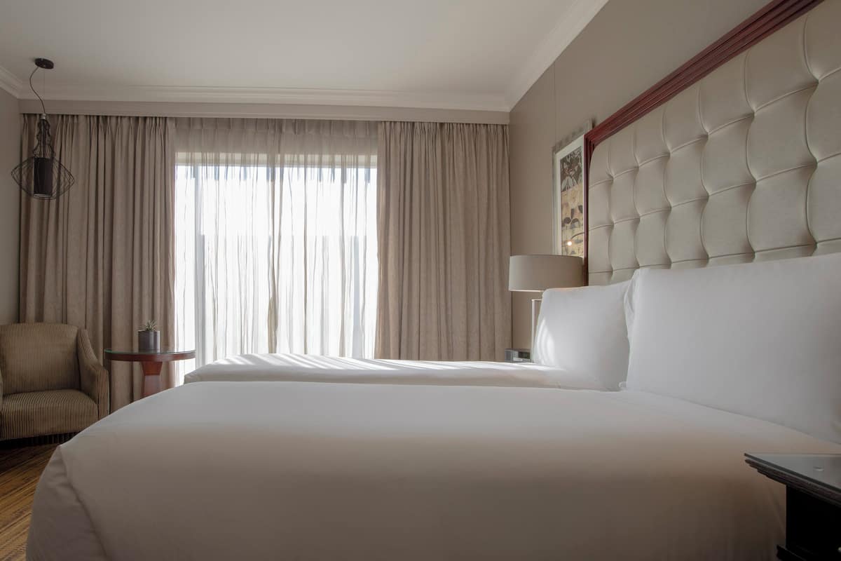 Une chambre d’hôtel avec un grand lit, une chaise, une table de chevet avec une lampe et une fenêtre avec des rideaux.