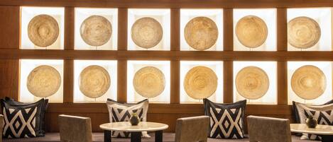 A seating area with round tables and chairs, arranged in rows with a wall of circular wooden panels behind.