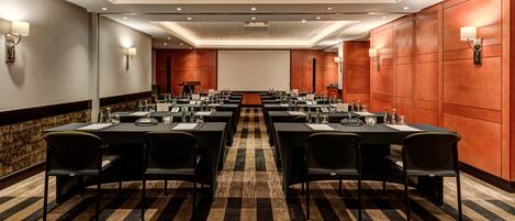 A conference room with long tables, chairs, and nameplates, equipped with water bottles and microphones.