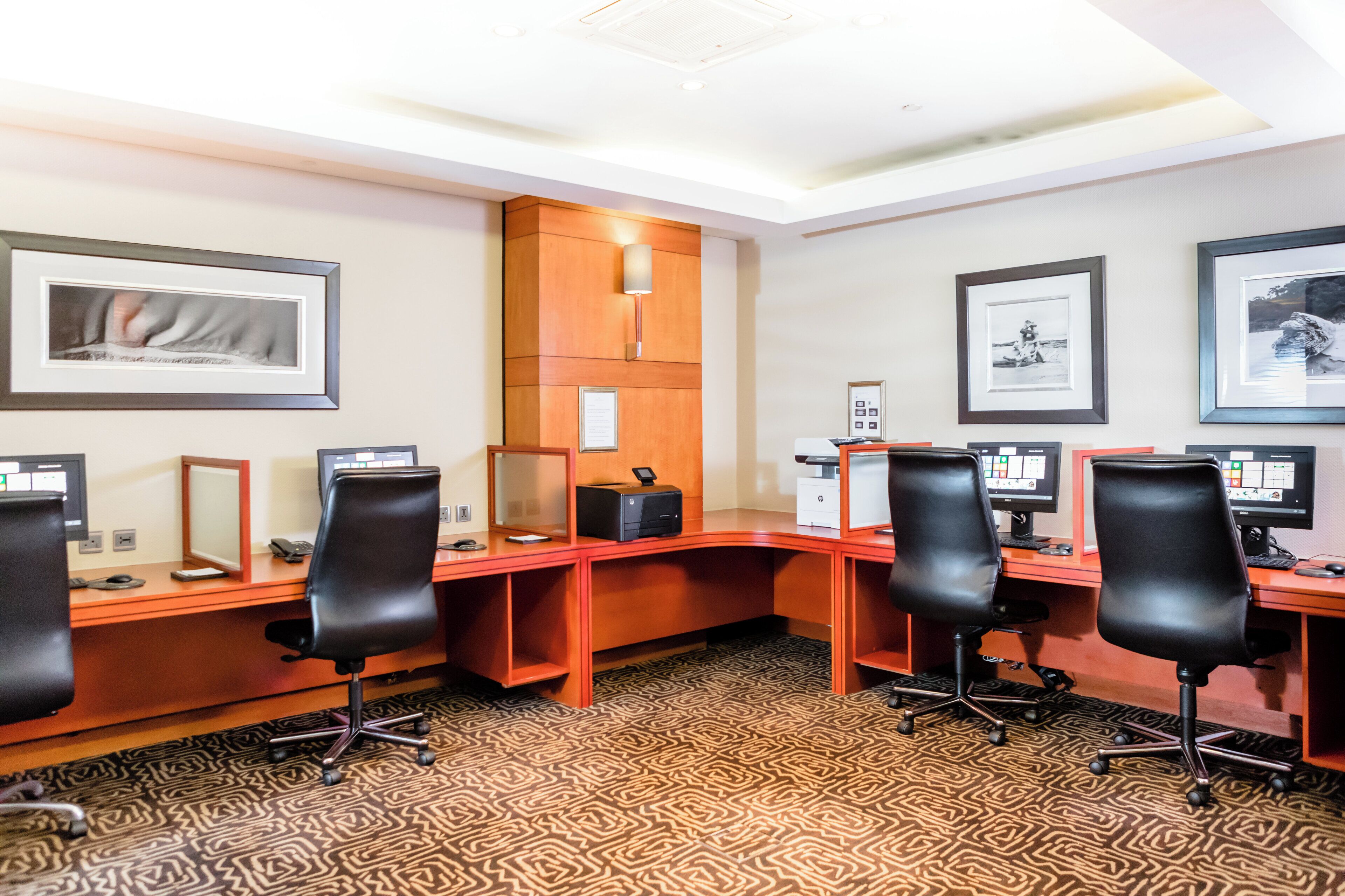 A conference room with four desks, each with a computer and a chair. There are framed pictures on the walls and a patterned carpet.