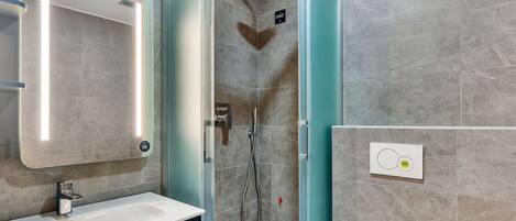 A modern bathroom with a glass-enclosed shower, a white sink, and a mirror with integrated lighting.