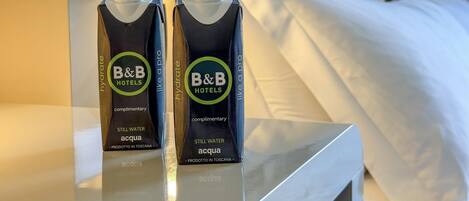Deux cartons de jus d’eau minérale de la marque B&B Hotels sont posés sur une table dans une chambre d’hôtel.