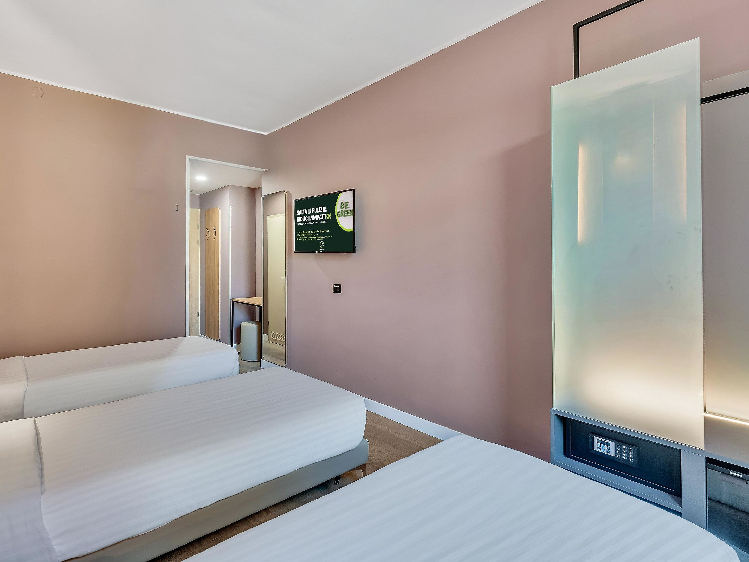 A hotel room with two beds, a mirror, a wall-mounted TV, and a sign promoting eco-friendly practices.