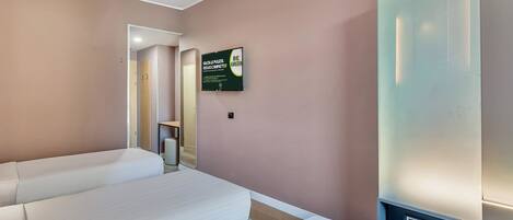 A hotel room with two beds, a mirror, a wall-mounted TV, and a sign promoting eco-friendly practices.