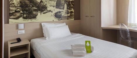 Una habitación de hotel con cama, mesita de noche, escritorio y un cuadro grande en la pared con un castillo.