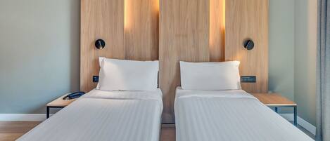 Habitación doble con dos camas, cabeceros de madera, mesitas de noche con lámparas y un teléfono en una de las mesitas.