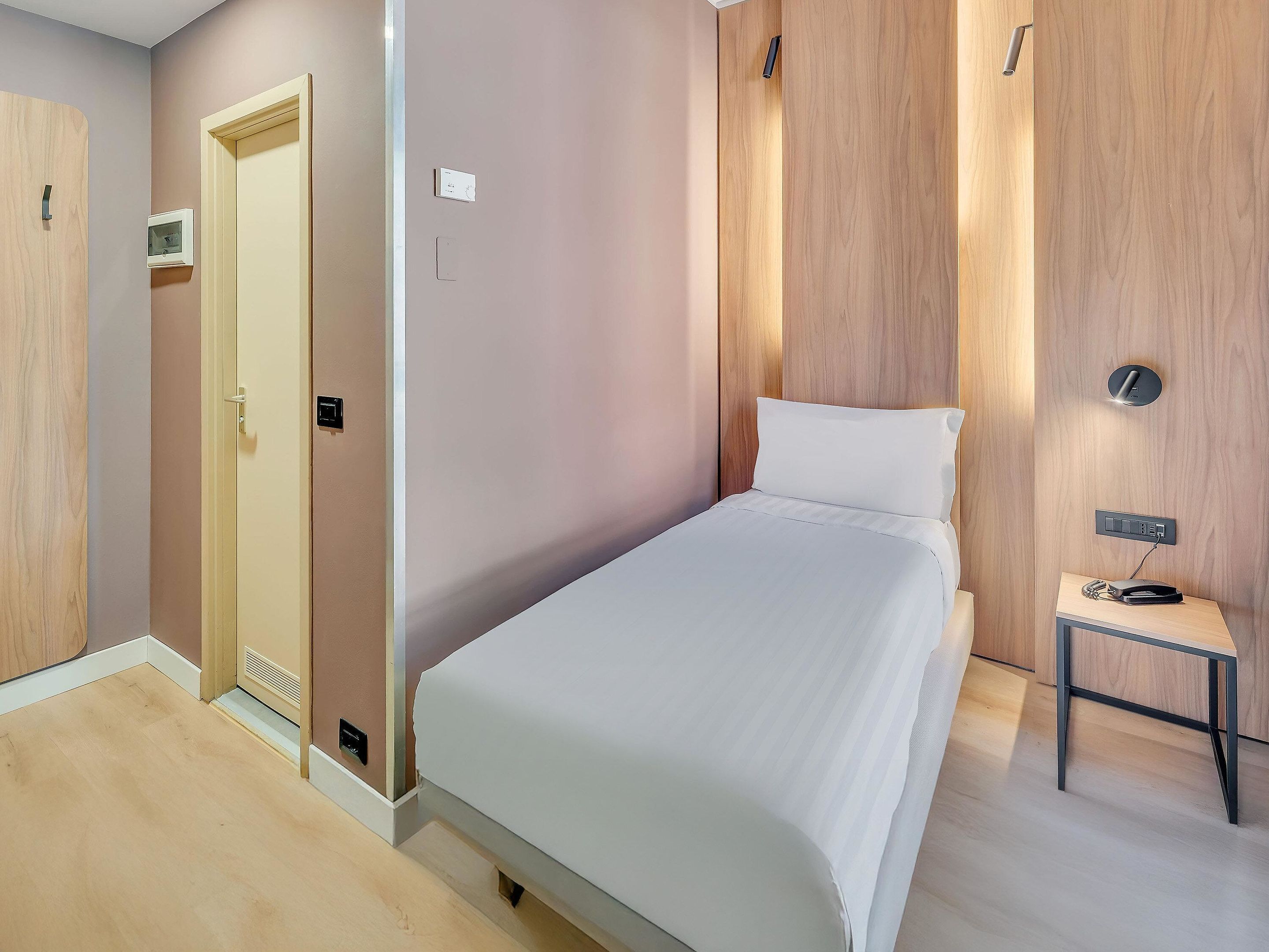 Une chambre d’hôtel moderne, équipée d’un lit, d’une table de chevet et d’une armoire en bois.