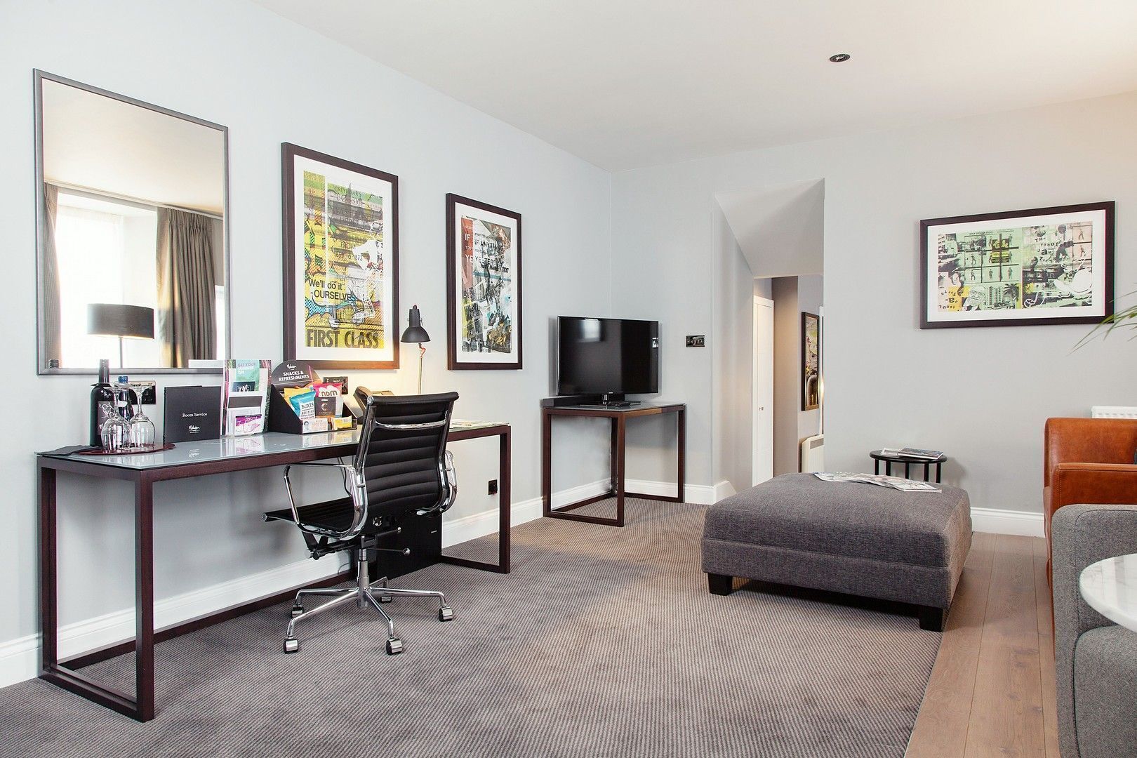 Habitación de hotel con escritorio, silla, televisor, cama y obras de arte en las paredes.