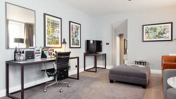 Habitación de hotel con escritorio, silla, televisor, cama y obras de arte en las paredes.