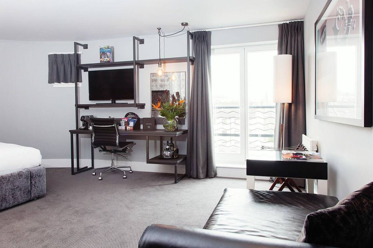 A modern hotel room with a bed, desk, chair, and a large window with curtains.