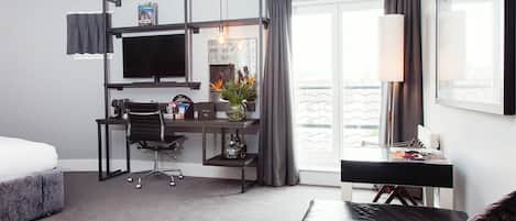 Una habitación de hotel moderna con cama, escritorio, silla y un ventanal con cortinas.