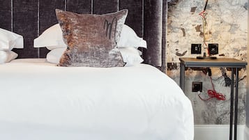 A neatly made bed with a dark headboard, a map-themed wallpaper, and a small bedside table with a lamp.