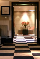 A checkered floor leading to a reception area with a framed sign, a radiator, and a vase with flowers.
