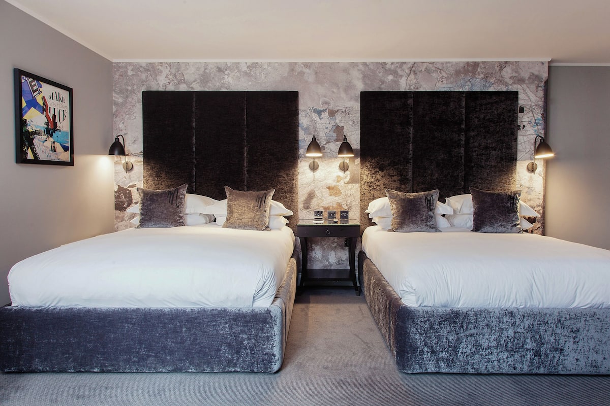 A double room with two beds, a small table, and wall-mounted lamps.