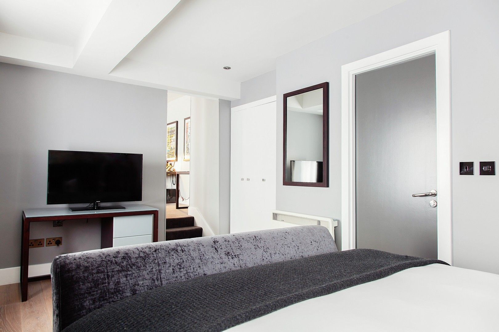 Una camera d'albergo moderna con un letto, una TV su una scrivania, uno specchio e una porta con un pannello di controllo.