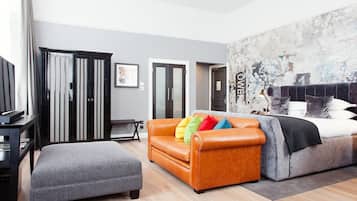 A modern hotel room with a grey sofa, a brown leather couch, a grey armchair, a bed with white and grey bedding, and a large abstract wall art piece.
