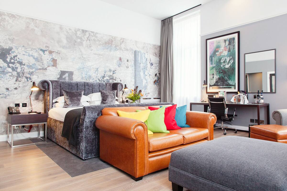 A modern bedroom with a bed, a sofa, a desk, and a large mirror.