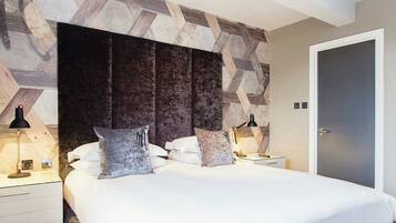 A bedroom with a bed, two bedside tables, a nightstand, and a door.