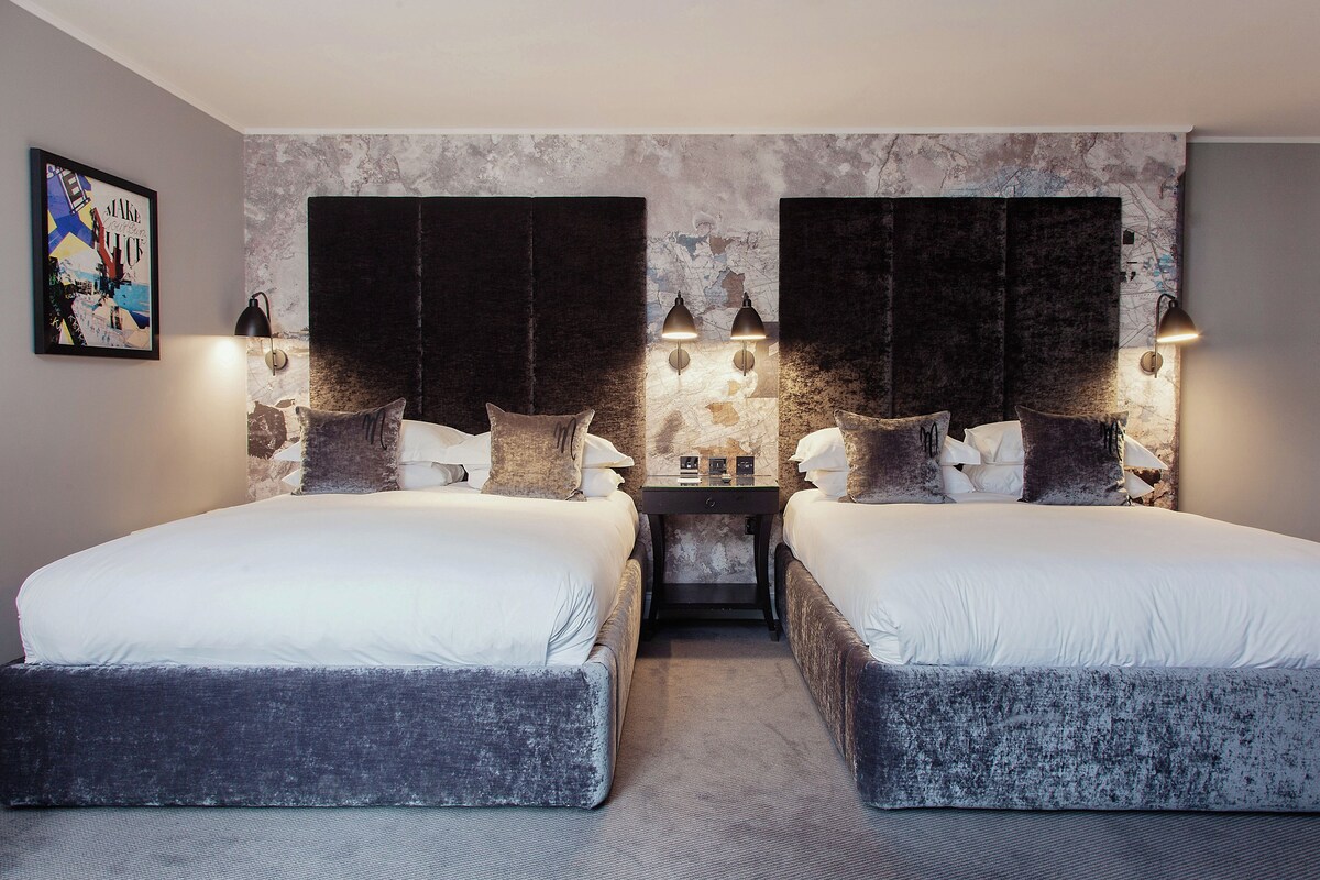 A double room with two beds, a small table, and wall-mounted lamps.