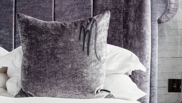 A bed with a grey upholstered headboard, white bedding, and a grey pillow with a monogram.