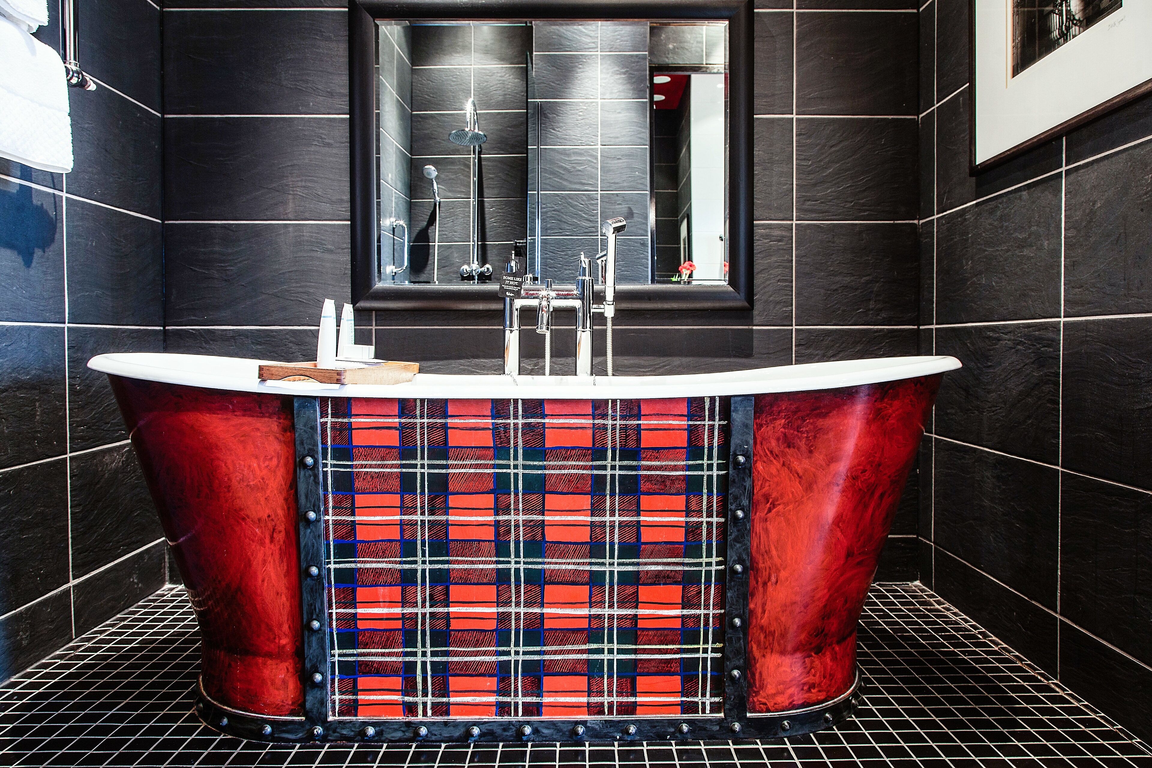 Un baño moderno con una bañera independiente, un espejo grande y paredes de azulejos negros.