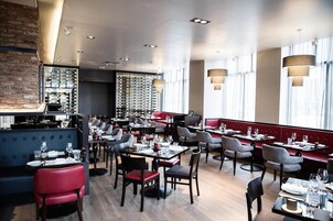 Un restaurant doté de plusieurs espaces de restauration, notamment des banquettes et des tables, avec un mur en briques et de grandes fenêtres.