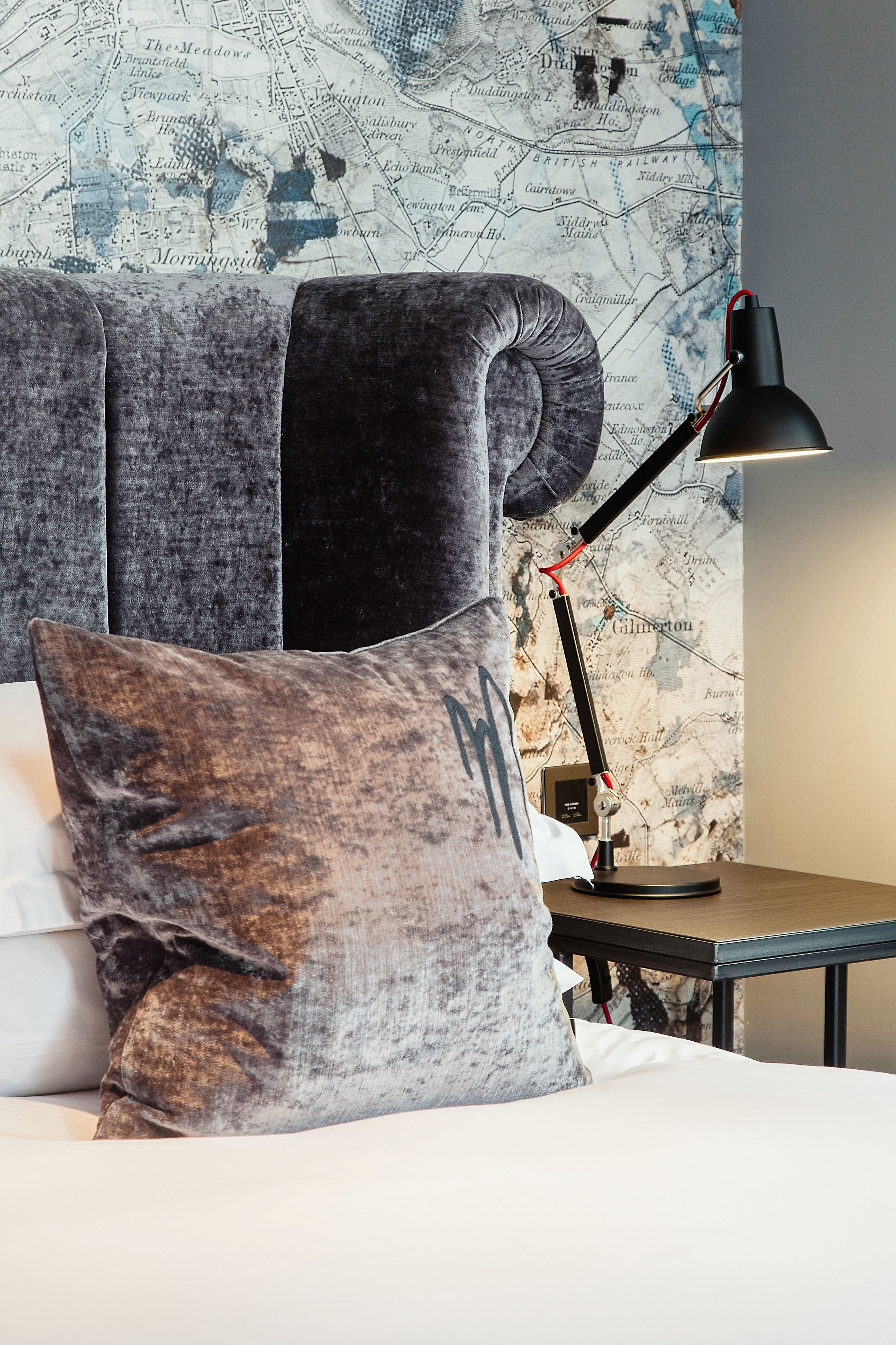 A bed with a map wallpaper, a dark lamp, and a textured pillow.