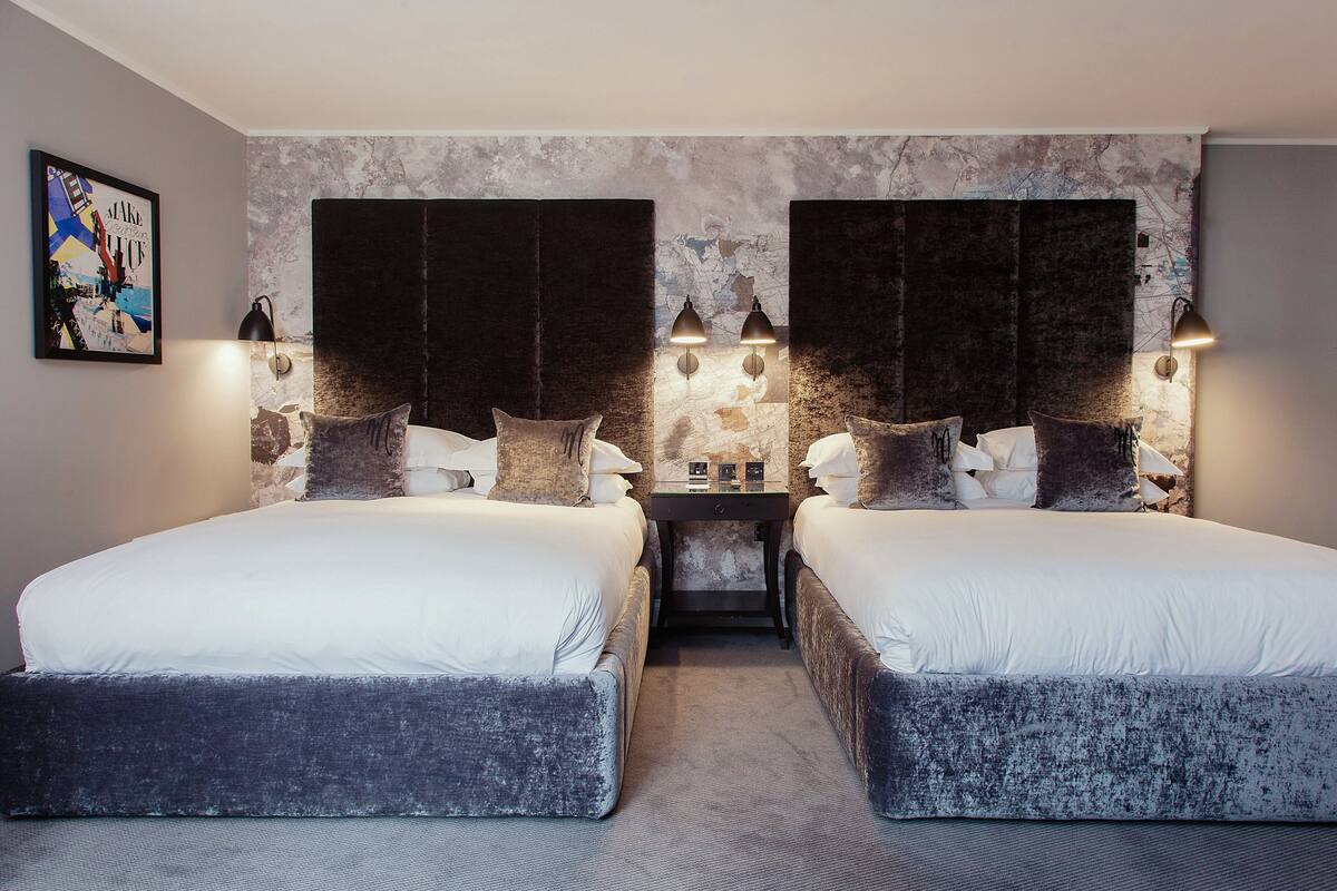A double room with two beds, a small table, and wall-mounted lamps.