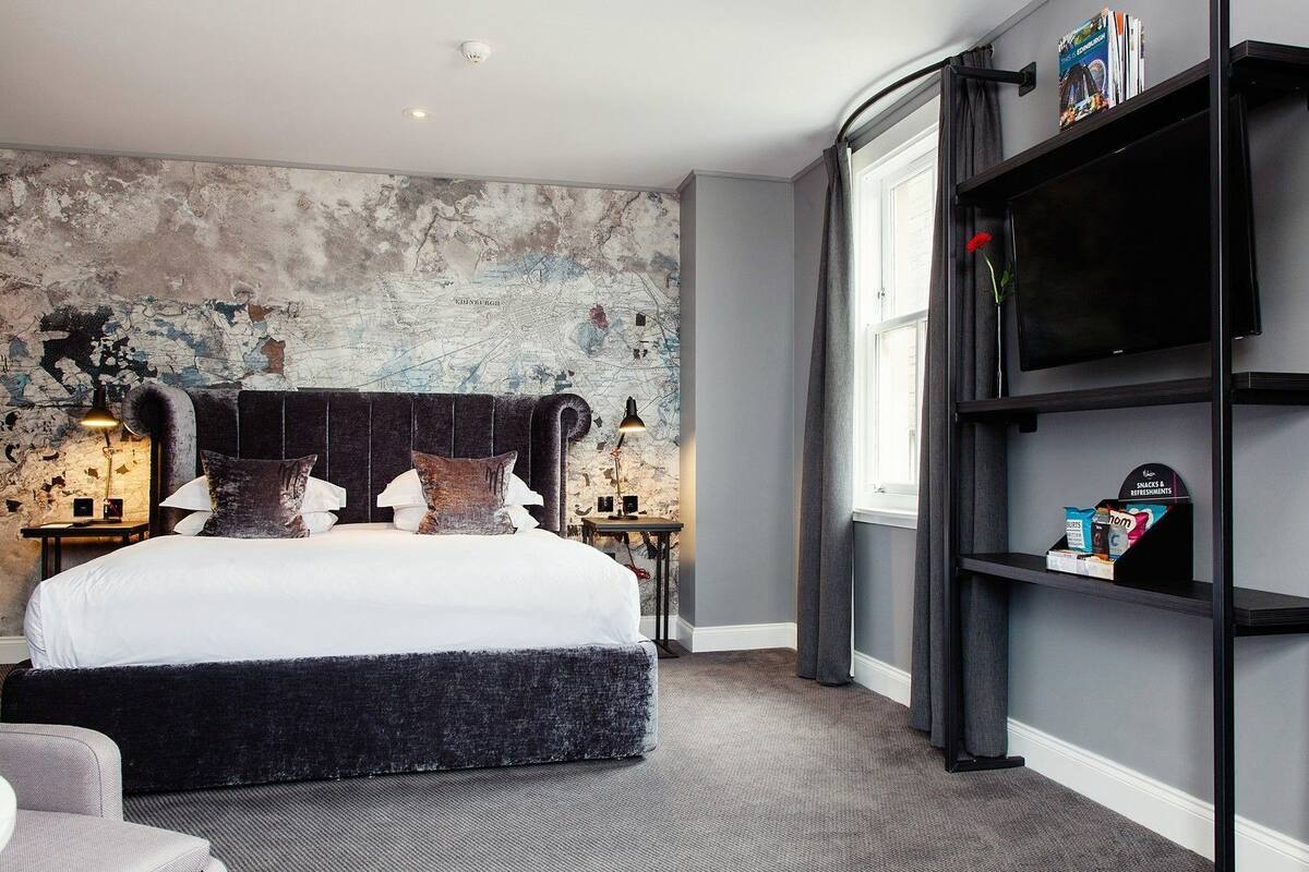 A bedroom with a large bed, a map mural on the wall, a bookshelf, and a window with curtains.