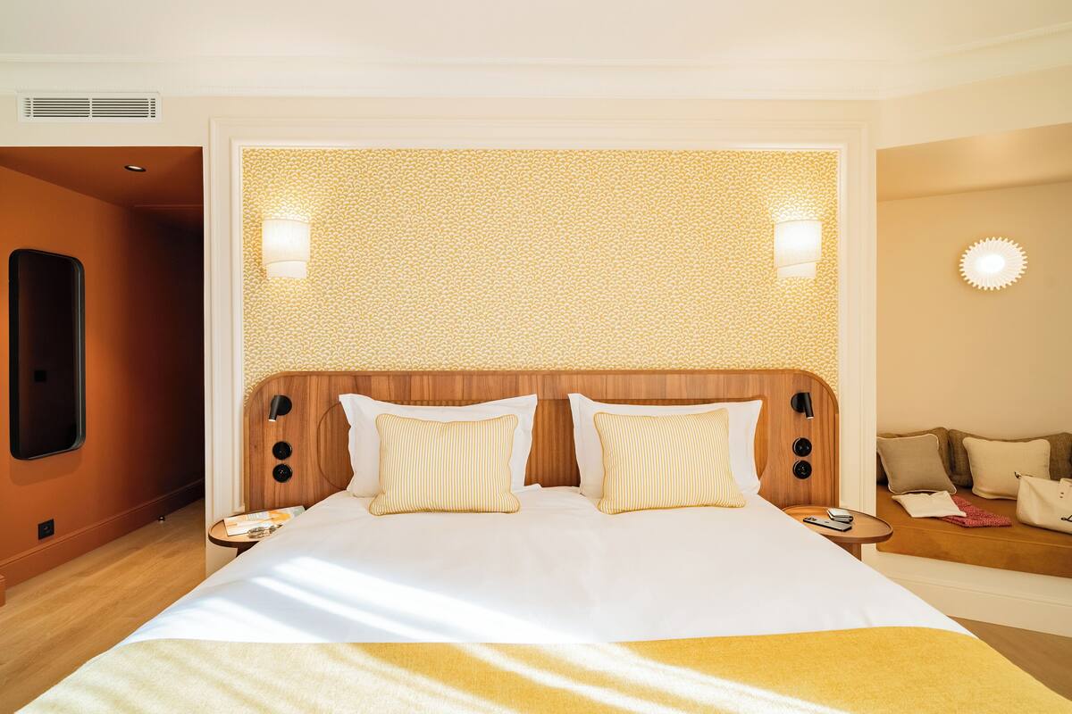 A hotel room with a large bed, bedside tables, a seating area, and a wall-mounted light fixture.