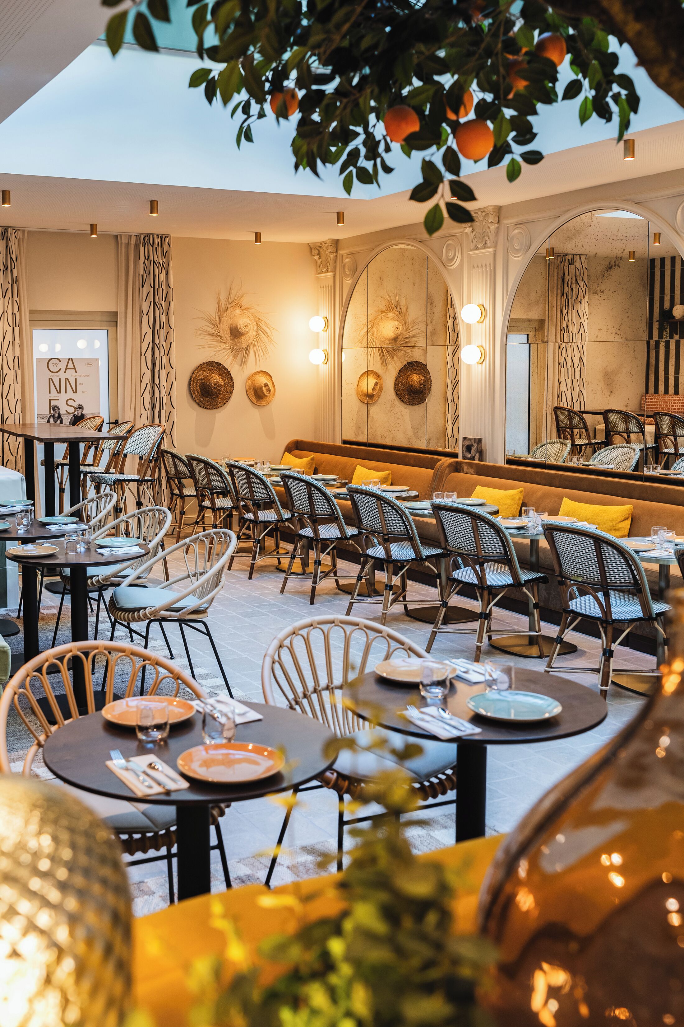 Un restaurant avec des tables rondes et des chaises en osier, un coin bar et un mur décoré de chapeaux.