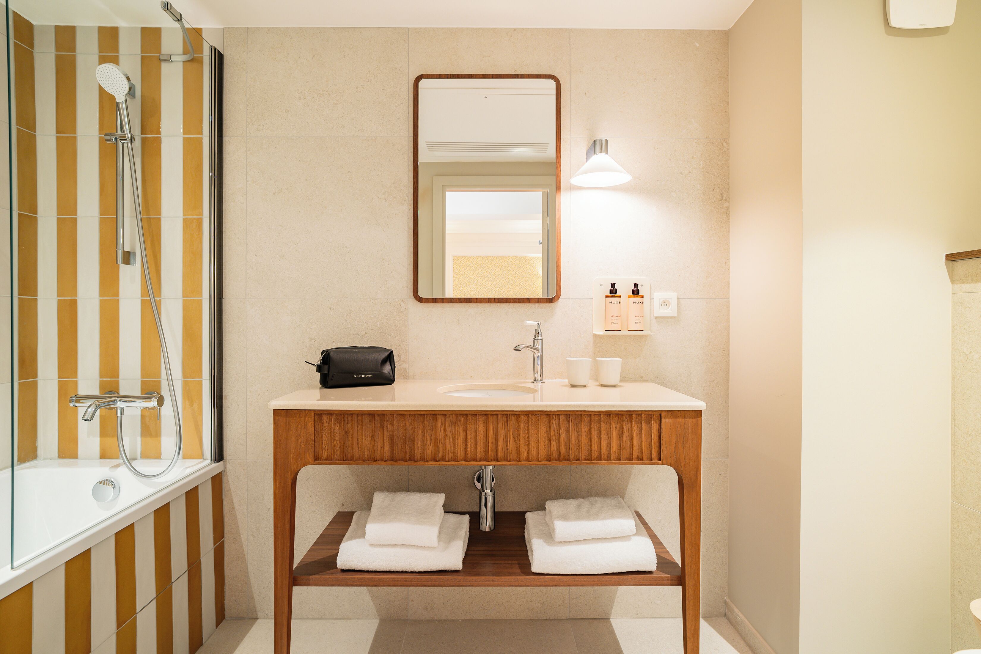 A bathroom with a shower, a sink, a mirror, and two towels on a shelf.