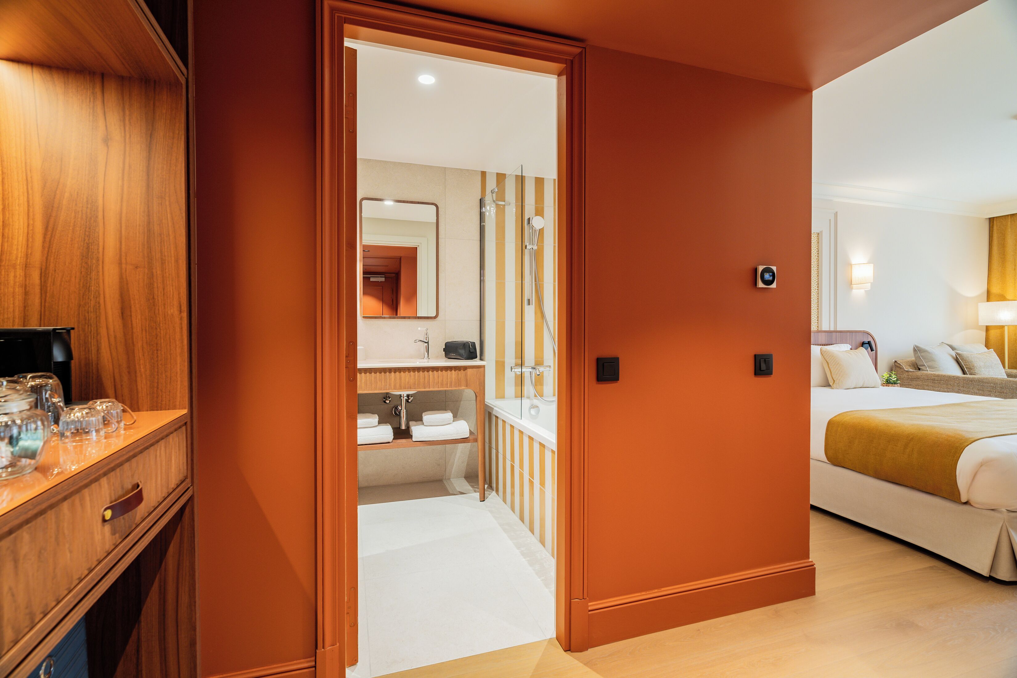 Habitación de hotel con un armario de madera, un baño con ducha y una cama con una colcha blanca y amarilla.