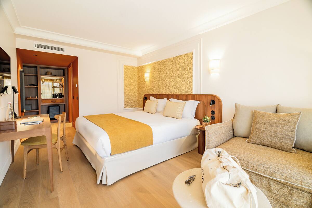 A hotel room with a bed, a desk, a chair, a sofa, and a small table with a lamp.