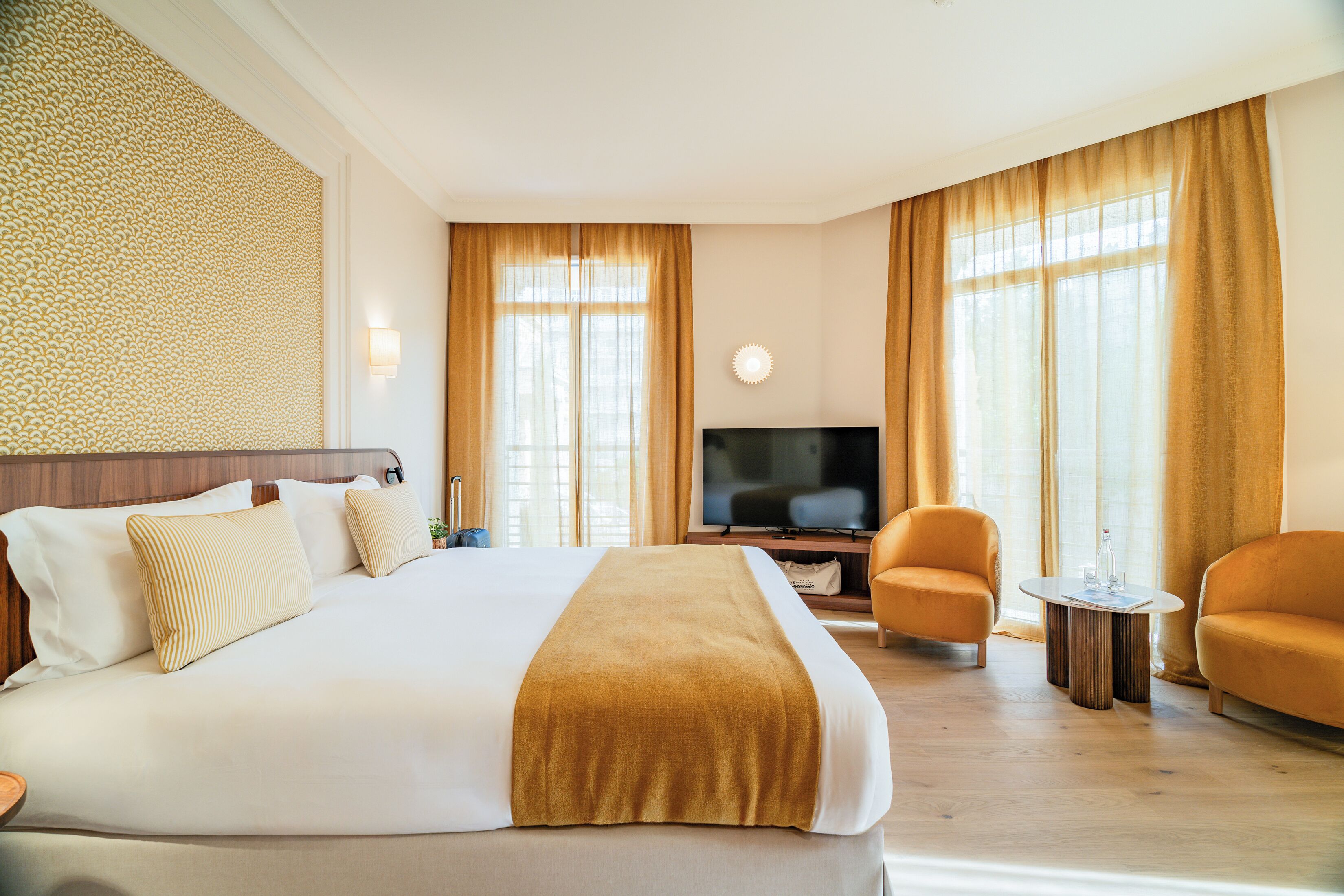 Una habitación de hotel con una cama grande, un televisor, dos sillones y una pequeña mesa.