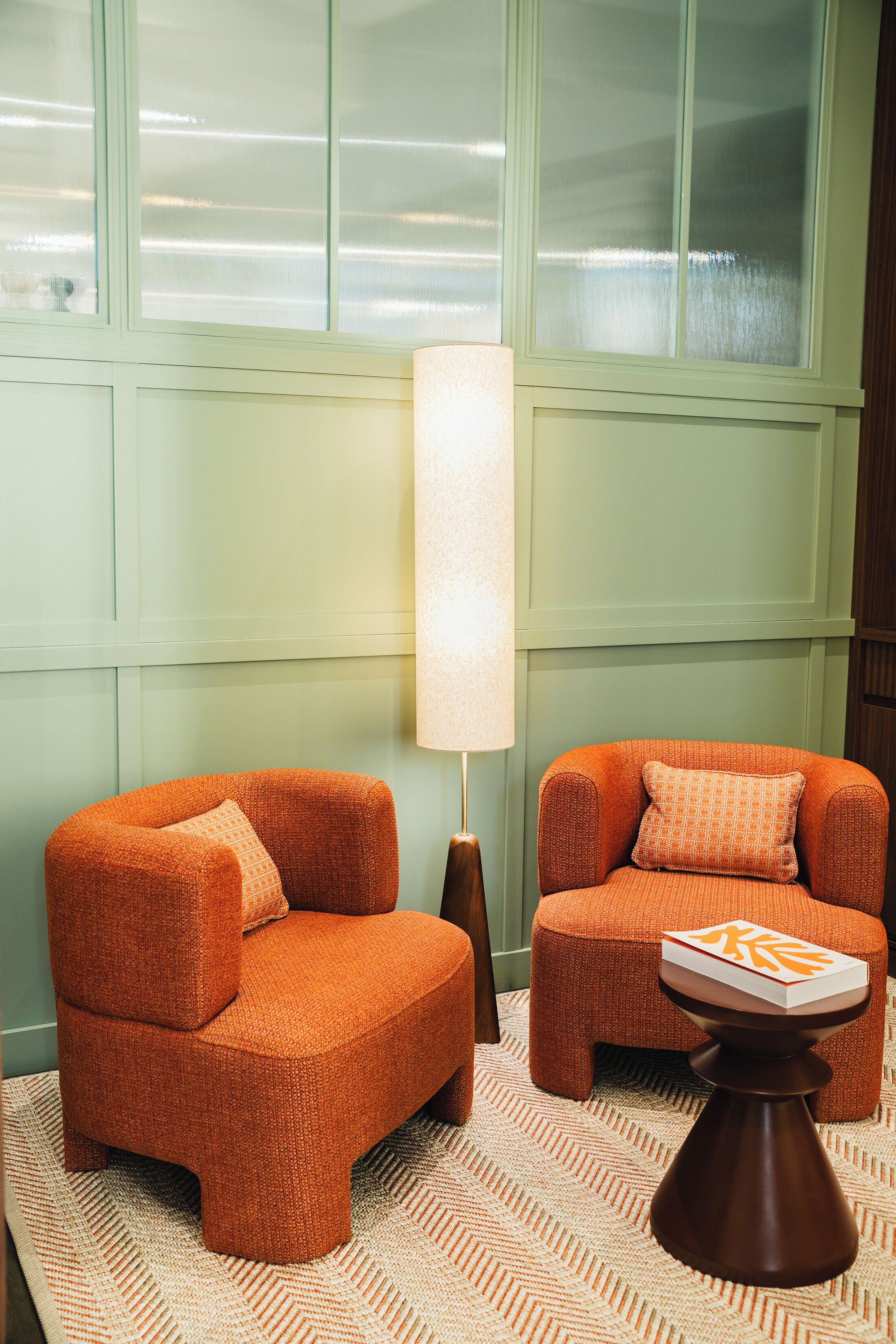 Una habitación con dos sillones naranjas, una lámpara de pie y un tapete estampado.